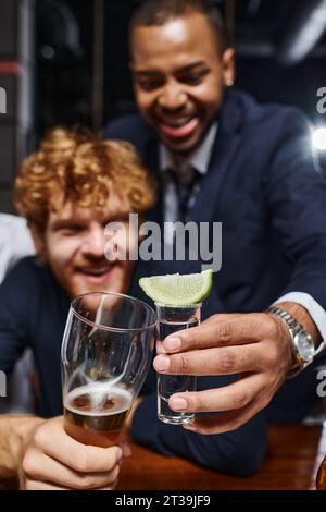 due colleghi interrazziali che dopo il lavoro bevono bicchieri al bar, un bicchierino di tequila e un bicchiere di birra Foto Stock