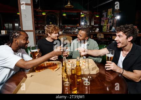 felici amici multietnici che scherzano, gestiscono e chiacchierano sulla pizza con birra, uomini alla festa del celibato Foto Stock