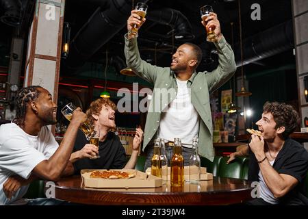 allegro afroamericano che prepara due bicchieri di birra vicino agli amici durante la festa di addio al celibato al bar Foto Stock