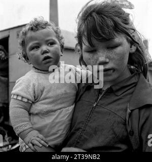 Giovane ragazza viaggiatrice che tiene un bambino tra le braccia fuori da una carovana durante l'evacuazione dei baraccopoli e la demolizione di St Ann's, Nottingham. 1969-1972, Foto Stock