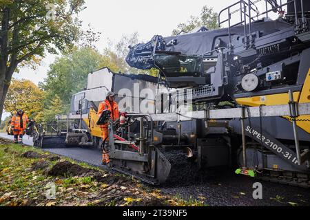 24 ottobre 2023, Brandeburgo, Schönow: La strada statale L 30 tra Schönow e Gorinsee (Barnim) è in fase di rinnovo con il metodo compatto dell'asfalto. Questo metodo, in cui vengono applicati contemporaneamente il legante per asfalto e la superficie dell'asfalto, consente di risparmiare tempo ed è anche più duraturo. Foto: Joerg Carstensen/dpa Foto Stock