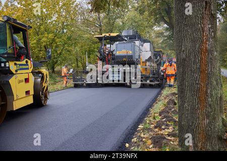 24 ottobre 2023, Brandeburgo, Schönow: La strada statale L 30 tra Schönow e Gorinsee (Barnim) è in fase di rinnovo con il metodo compatto dell'asfalto. Questo metodo, in cui vengono applicati contemporaneamente il legante per asfalto e la superficie dell'asfalto, consente di risparmiare tempo ed è anche più duraturo. Foto: Joerg Carstensen/dpa Foto Stock