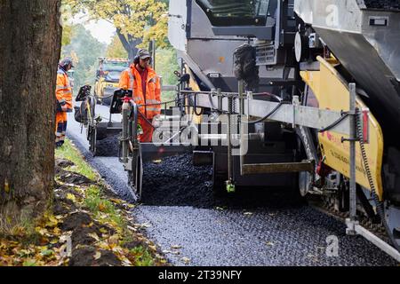 24 ottobre 2023, Brandeburgo, Schönow: La strada statale L 30 tra Schönow e Gorinsee (Barnim) è in fase di rinnovo con il metodo compatto dell'asfalto. Questo metodo, in cui vengono applicati contemporaneamente il legante per asfalto e la superficie dell'asfalto, consente di risparmiare tempo ed è anche più duraturo. Foto: Joerg Carstensen/dpa Foto Stock