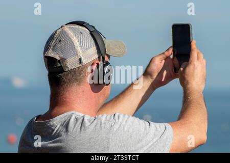 uomo di mezza età che indossa un berretto da baseball con cuffie e scatta una foto o una fotografia con uno smartphone. Foto Stock