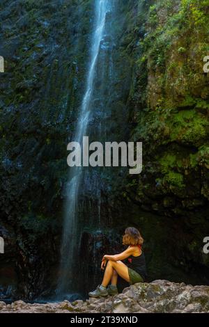 Unbekannte junge Frau sitzt im Wasserfall an der Levada do Caldeirao Verde, Queimadas, Madeira Foto Stock