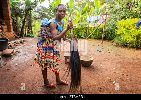 La giovane madre africana con il suo bambino legato alla schiena in un loincloth che le tiene una coda di cavallo tra le mani. Foto Stock