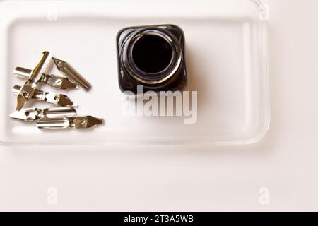 flacone di inchiostro con punte metalliche per penna su sfondo bianco. cancelleria sulla scrivania bianca, vista dall'alto. lezioni di ortografia ed esercizi di caligrafia. T Foto Stock