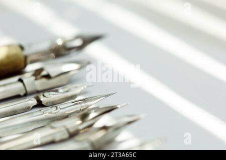 punte metalliche per la penna su sfondo bianco a raggi solari. cancelleria sulla scrivania bianca, vista dall'alto. lezioni di ortografia ed esercizi di caligrafia. Foto Stock