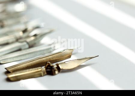 punte metalliche per la penna su sfondo bianco a raggi solari. cancelleria sulla scrivania bianca, vista dall'alto. lezioni di ortografia ed esercizi di caligrafia. Foto Stock