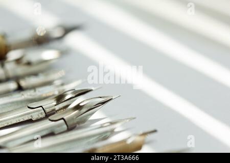 punte metalliche per la penna su sfondo bianco a raggi solari. cancelleria sulla scrivania bianca, vista dall'alto. lezioni di ortografia ed esercizi di caligrafia. Foto Stock