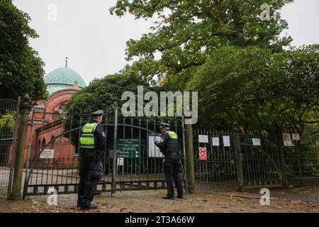 Amburgo, Germania. 24 ottobre 2023. Due agenti di pattuglia del dipartimento di polizia responsabile parlano con un impiegato del cimitero all'ingresso chiuso del cimitero ebraico di Amburgo-Ohlsdorf. Per motivi di sicurezza e paura di atti vandalici, il cimitero ebraico di Amburgo è stato chiuso al pubblico. Credito: Christian Charisius/dpa/Alamy Live News Foto Stock