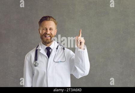 Un allegro medico maschio sorridente alza il dito come segno che ha una buona idea. Foto Stock