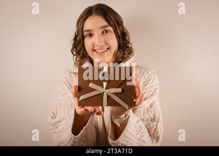 Donna che guarda la fotocamera e tiene in mano il buono regalo. busta in bronzo fatta a mano con fiocco Foto Stock