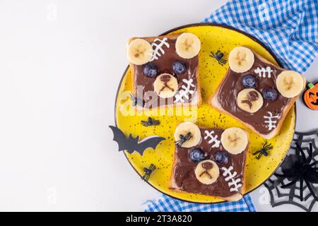 Buffi panini toast all'orso di Halloween con burro di noci, pasta, banana e marshmallow fuso o cicatrici di yogurt. Pranzo creativo di Halloween Foto Stock
