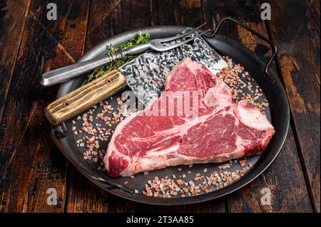 Bistecca alla fiorentina cruda o bistecca all'osso T, carne di manzo in marmo in un vassoio da cucina in acciaio Sfondo di legno. Vista dall'alto. Foto Stock