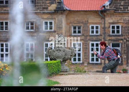 Blankenburg, Germania. 24 ottobre 2023. Una donna scatta una foto nel giardino barocco del piccolo castello di Blankenburg. Come giardino principesco di piacere, questo parco è stato costruito intorno al 1725. Il parco dispone di quattro terrazze, che invitano i visitatori con fontane, sculture in arenaria, piantagioni, panchine e sentieri. Nei prossimi giorni le condizioni meteorologiche rimarranno variabili. Crediti: Matthias Bein/dpa/Alamy Live News Foto Stock