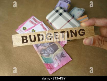La parola budgeting è incisa su un blocco di legno con il denaro sullo sfondo. Rupiah indonesiana. Concetto di budget. copia spazio Foto Stock