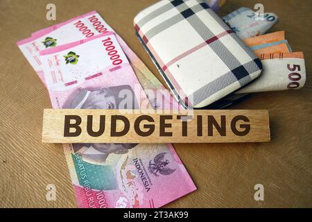 La parola budgeting è incisa su un blocco di legno con il denaro sullo sfondo. Rupiah indonesiana. Concetto di budget. copia spazio Foto Stock
