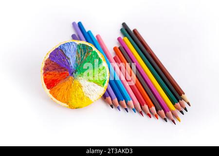 Arcobaleno colorato a metà frutta arancione accanto a pastelli multicolori, isolati su bianco Foto Stock