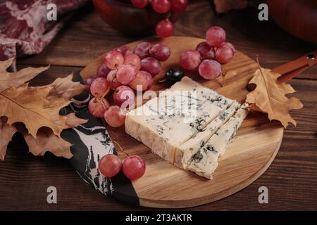 Piatto di formaggi servito con frutta autunnale e foglie secche Foto Stock