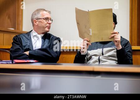 Oldenburg, Germania. 24 ottobre 2023. L'imputato (r) siede accanto al suo avvocato Andreas Lauven in un'aula di tribunale presso il tribunale regionale prima dell'inizio del processo, tenendo una copertura davanti al suo volto. Secondo le indagini, l'uomo avrebbe ucciso un altro paziente nell'aprile 2023 in una clinica a Bad Zwischenahn con una massiccia violenza contro il collo. Durante il processo, l'imputato ha negato il crimine. Credito: Hauke-Christian Dittrich/dpa/Alamy Live News Foto Stock