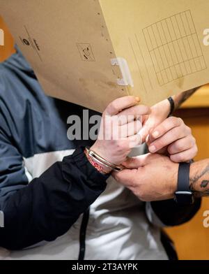 Oldenburg, Germania. 24 ottobre 2023. Prima dell'inizio del processo, l'imputato siede in un'aula del tribunale regionale con manette e ha una copertura davanti al suo volto. Secondo le indagini, l'uomo avrebbe ucciso un altro paziente nell'aprile 2023 in una clinica a Bad Zwischenahn con una forza massiccia contro il collo. Durante il processo, l'imputato ha negato il crimine. Credito: Hauke-Christian Dittrich/dpa/Alamy Live News Foto Stock