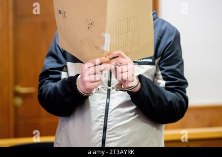 Oldenburg, Germania. 24 ottobre 2023. Prima dell'inizio del processo, l'imputato si trova in un'aula del tribunale regionale con le manette e ha una copertura davanti al suo volto. Secondo le indagini, l'uomo avrebbe ucciso un altro paziente nell'aprile 2023 in una clinica a Bad Zwischenahn con una forza massiccia contro il collo. Durante il processo, l'imputato ha negato il crimine. Credito: Hauke-Christian Dittrich/dpa/Alamy Live News Foto Stock