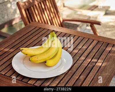 Banane fresche su un piatto bianco su un tavolo da giardino in legno. Foto Stock