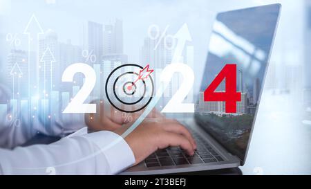 L'uomo d'affari sta usando un computer e mostra le lettere 2024 che rappresentano gli obiettivi per l'anno 2024 e il concetto di avviare un'attività insieme Foto Stock