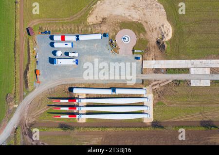 Vista aerea del cantiere che mostra le parti delle turbine eoliche come le enormi pale del rotore e le sezioni delle torri in acciaio per l'assemblaggio del mulino a vento presso il parco eolico Foto Stock