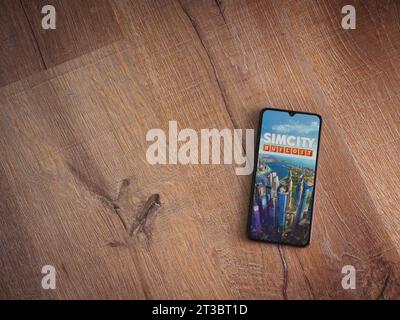 LOD, Israele - 16 luglio 2023: Schermata di avvio dell'app SimCity BuildIt sullo smartphone su sfondo ligneo. Vista dall'alto con spazio per la copia. Foto Stock