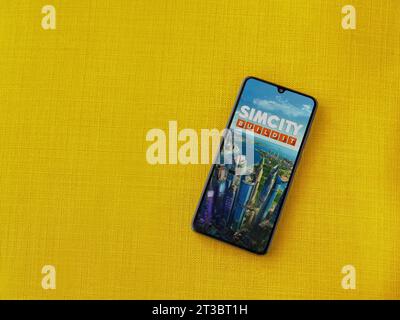 LOD, Israele - 16 luglio 2023: Schermata di avvio dell'app SimCity BuildIt sullo smartphone su sfondo giallo. Vista dall'alto con spazio per la copia. Foto Stock