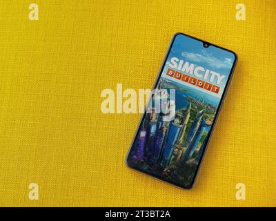 LOD, Israele - 16 luglio 2023: Schermata di avvio dell'app SimCity BuildIt sullo smartphone su sfondo giallo. Vista dall'alto con spazio per la copia. Foto Stock