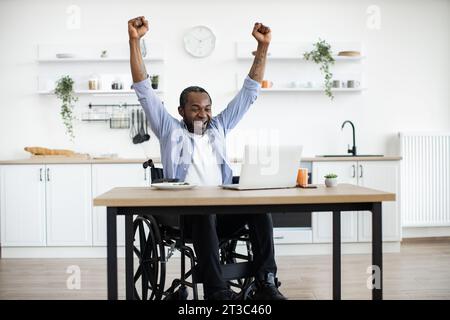 L'utilizzatore africano di sedia a rotelle celebra il successo alzando le mani Foto Stock