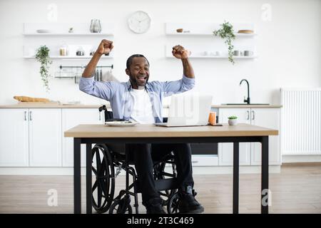 African wheelchair user celebrating success by raising hands up Stock Photo