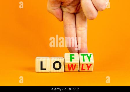 Simbolo alto o basso. Parole concettuali Lofty lowly su blocco di legno. Bellissimo sfondo arancione. Mano d'affari. Affari alti o bassi Foto Stock