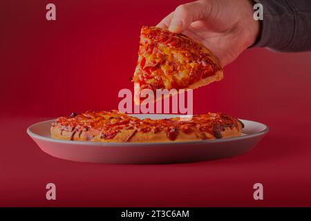 Pizza in padella fresca e carina, con un pezzo da tenere su uno sfondo rosso. Foto Stock