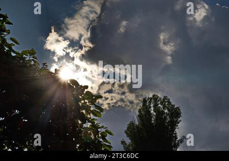 Sfondo di nuvole piovose e soffici che fluttuano in un cielo blu con un sole luminoso che splende tra di loro, Sofia, Bulgaria Foto Stock