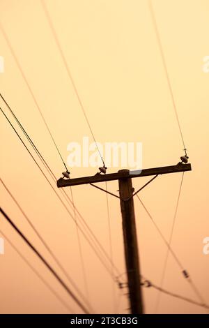 Palo e linee elettriche contro il cielo arancione Foto Stock