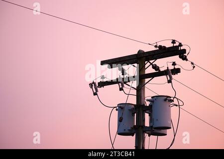 Palo di servizio con trasformatori di distribuzione contro il cielo rosa Foto Stock