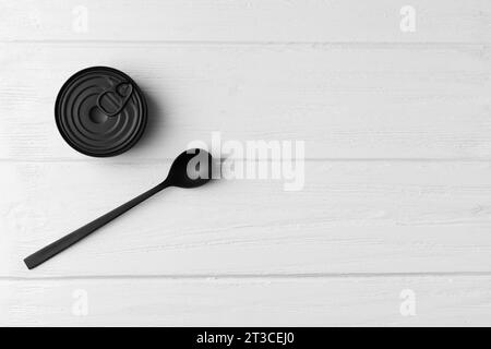 Latta chiusa rotonda opaca nera e cucchiaio nero su sfondo di legno grigio, vista dall'alto con spazio per testo, cibo in scatola, conserve. Foto Stock