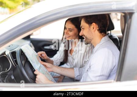 Coppia sorridente che guarda una mappa cartacea seduto all'interno dell'auto Foto Stock