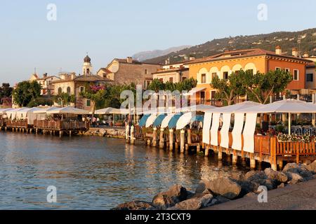 Terrazza ristorante con ombrelloni sulla riva del lago, sole serale, Torri del Benaco, riva orientale del Lago di Garda, provincia di Verona, Italia Foto Stock