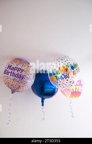 quattro palloncini all'elio decorati con puntini colorati e un messaggio di buon compleanno, con un nastro appeso, sul tetto di una stanza bianca, sfondo degradato Foto Stock