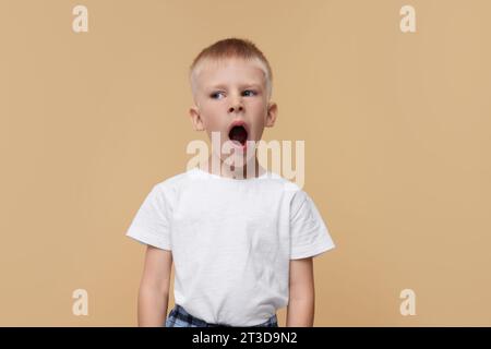 Un ragazzo assonnato che sbadiglia su sfondo beige. Problema di insonnia Foto Stock