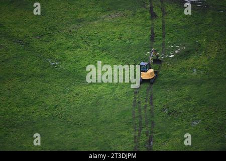 Prospettiva aerea di una scavatrice gialla impegnata in attività agricole all'interno del paesaggio rurale. Foto Stock