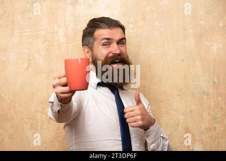 Buon giorno. L'uomo tiene una tazza di caffè. Tè del mattino. Buon giorno. Un uomo con una tazza di tè. Uomo hipster con una tazza di caffè. L'uomo barbuto sorridente tiene la tazza di tè Foto Stock