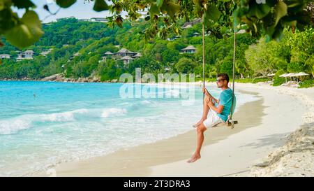 Giovani uomini che si rilassano in un'altalena sulla spiaggia delle isole tropicali delle Seychelles di Mahe. Uomo in una vacanza di lusso alle Seychelles Foto Stock