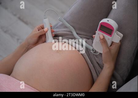 Primo piano della pancia di una donna incinta usando un doppler domestico. Schermo vuoto. Foto Stock