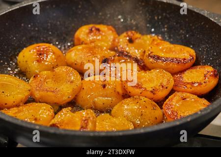 Le metà delle albicocche fresche vengono fritte in sciroppo di caramello in padella sul fornello a gas Foto Stock